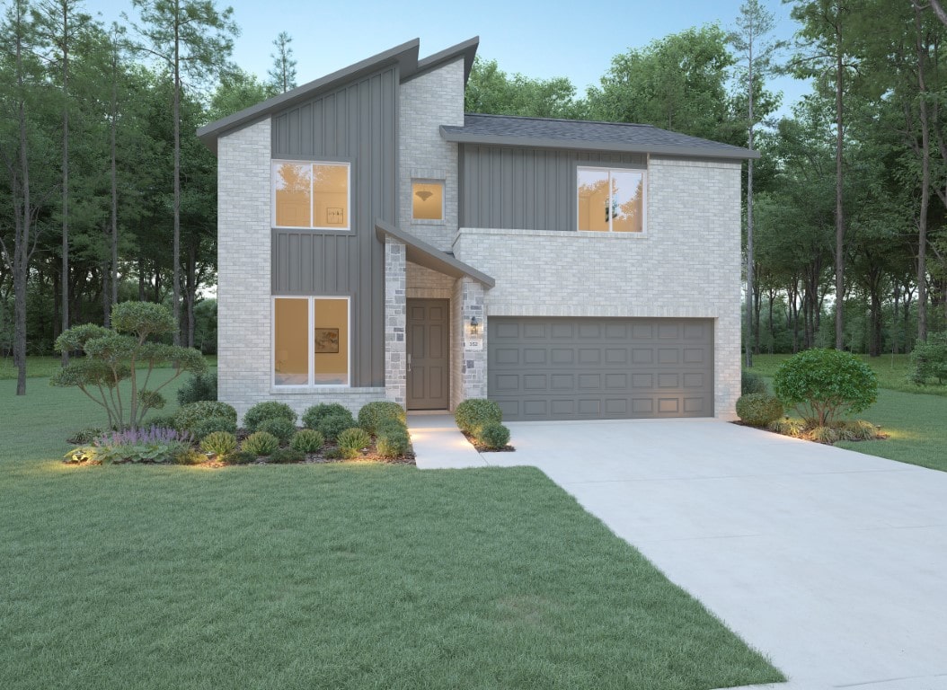 Modern two-story house with light brick and gray paneling, large windows, and a double garage. The yard is landscaped with bushes and small trees, and a wide driveway leads to the garage. Tall trees are in the background.
