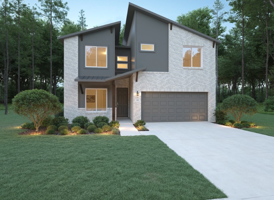 Modern two-story house with light brick exterior, dark gray accents, and large windows. There’s a double garage, landscaped shrubs, and a wide driveway, all surrounded by a green lawn and tall trees in the background.