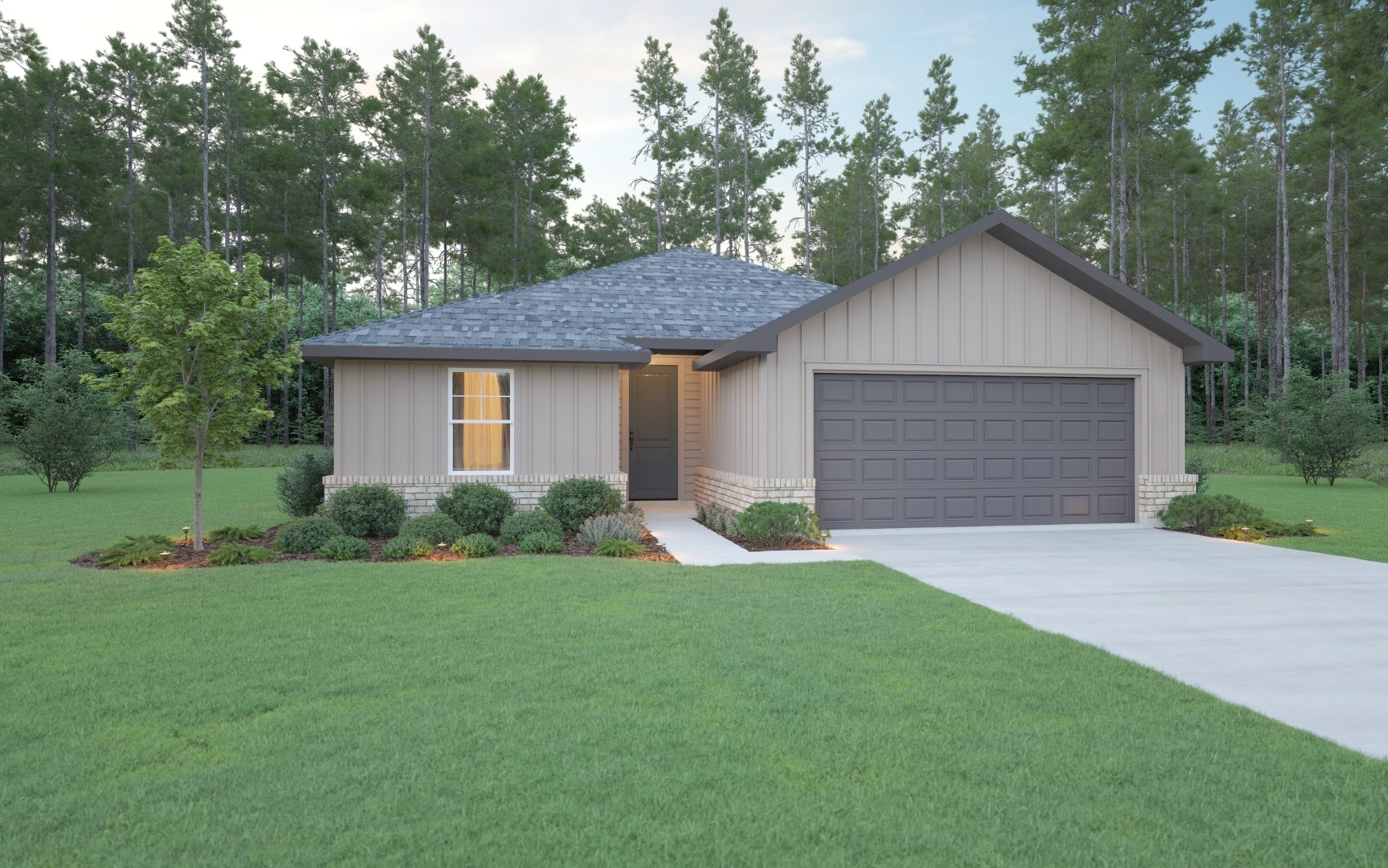 A small, single-story house with gray siding, a dark gray roof, and a two-car garage sits on a green lawn with shrubs, a young tree, and a concrete driveway, surrounded by tall pine trees in the background.