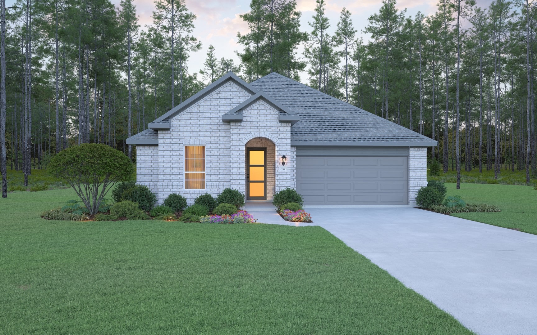 A single-story brick house with a gray roof, two-car garage, front porch light on, neatly trimmed bushes, flower beds, and a wide driveway, set against a backdrop of tall trees and a large green lawn.