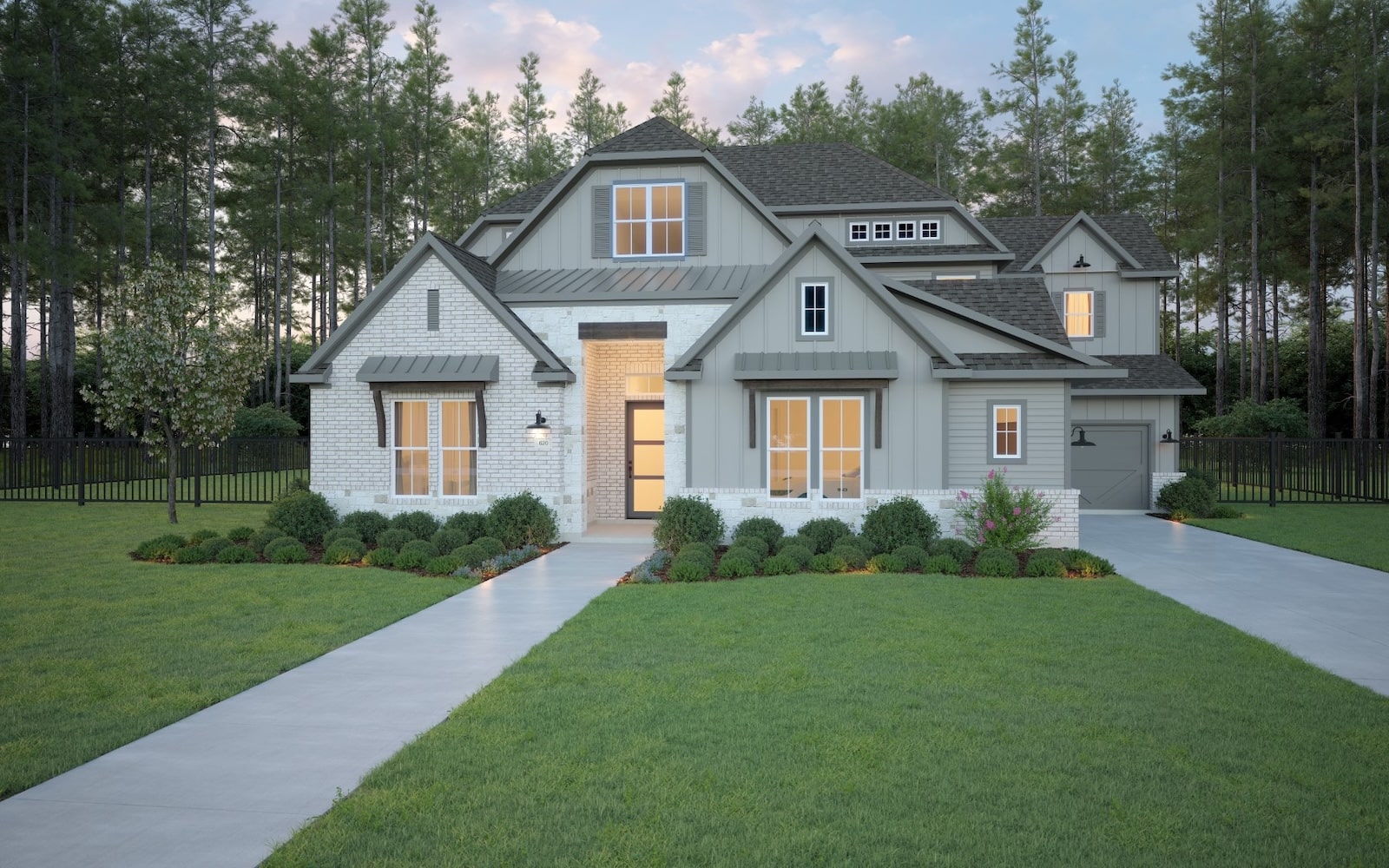 Modern two-story house with gray siding and white brick, large windows, a well-kept lawn, manicured shrubs, and concrete walkways leading to the front entrance, surrounded by tall pine trees at sunset.
