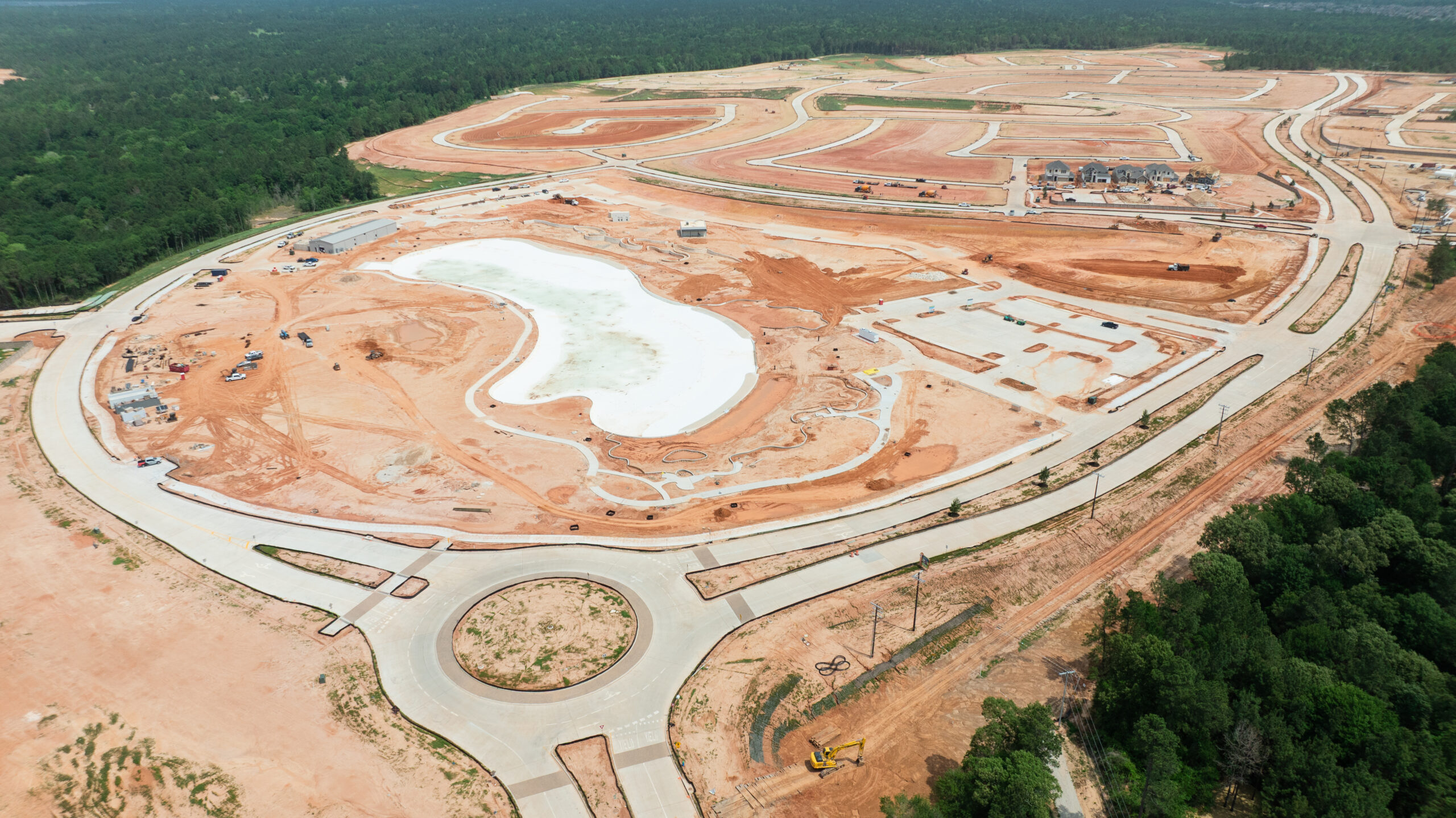 Aerial view of Grand magnolia community in Magnolia, TX under construction, with roads, roundabout, cleared land, and a central lagoon.