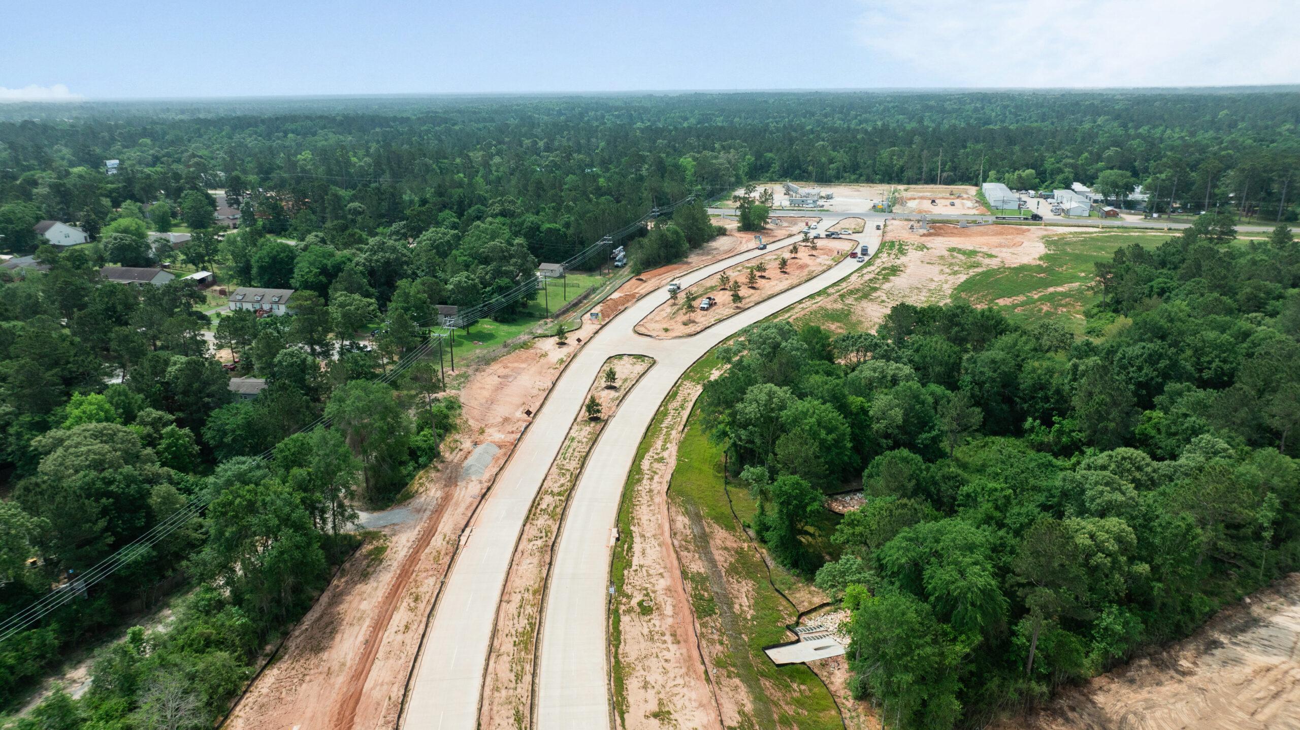 Aerial view of Grand Magnolia community in Magnolia, TX through a green, forested area, with a finished roadway.