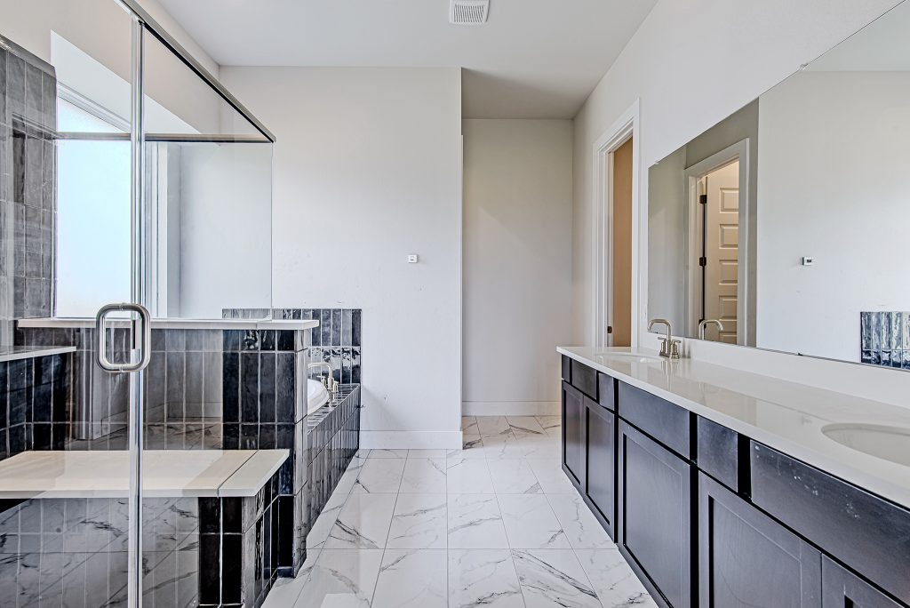 Modern bathroom with a glass-enclosed shower, dark wood cabinets, double sinks, large mirror, marble tile floor, and a bathtub partially visible on the left. Walls are light-colored, creating a bright, clean look.