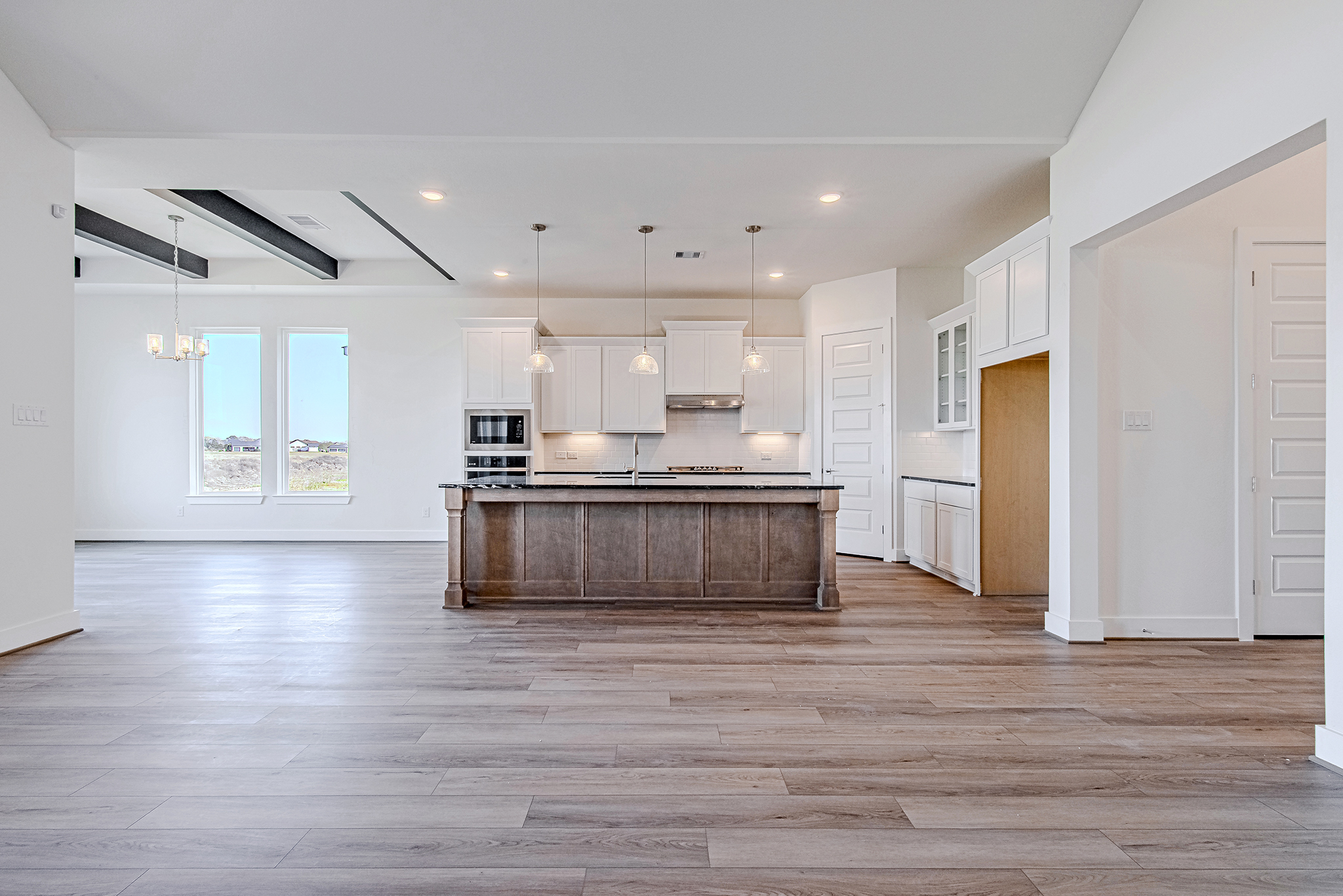 Modern open-concept kitchen and dining area with light wood flooring, white cabinets, a large center island with pendant lights, and large windows letting in natural light.