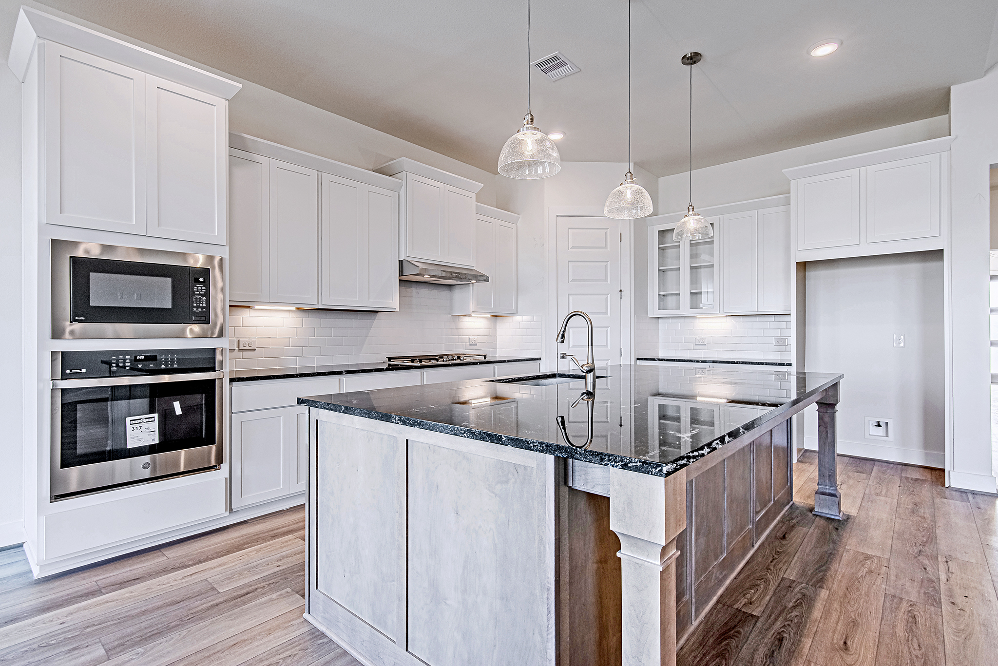 Modern kitchen with white cabinets, stainless steel appliances, a large black granite island, pendant lights, light wood flooring, and subway tile backsplash. The space is bright, spacious, and contemporary in design.