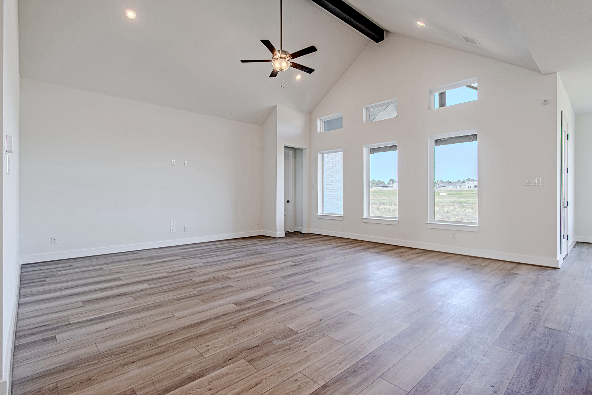 Spacious empty room with vaulted ceiling, light wood flooring, white walls, a ceiling fan, and multiple tall windows letting in natural light.